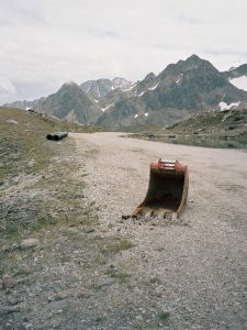 Rohre und Baggerschaufel liegen auf Strasse vor Bergpanorama