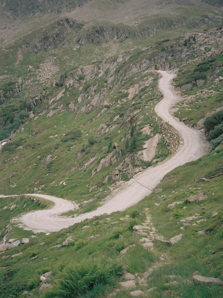 Steile Schotterstrasse durch grüne Bergvegetation